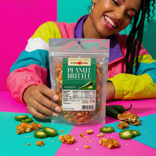 Person holding a package of Jalapeno Peanut Brittle against a colorful background